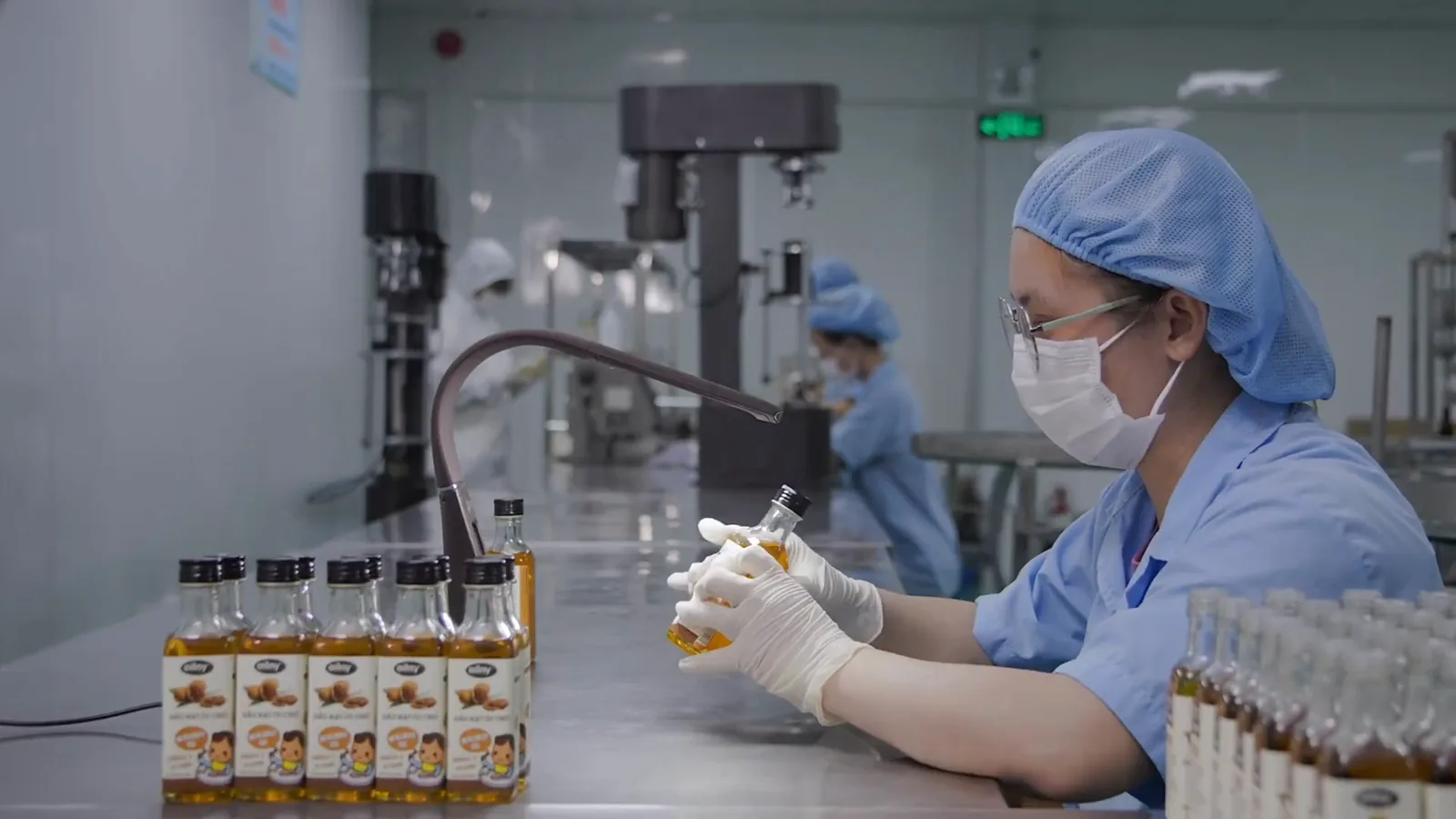 Nhân viên nhà máy cầm chai dầu Oilny soi kiểm tra trên bàn dây chuyền